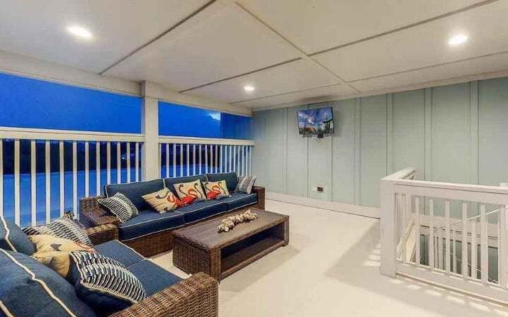 Your covered terrace offers panoramic views through floor-to-ceiling windows. Sink into plush wicker seating with colorful pillows for ultimate relaxation.