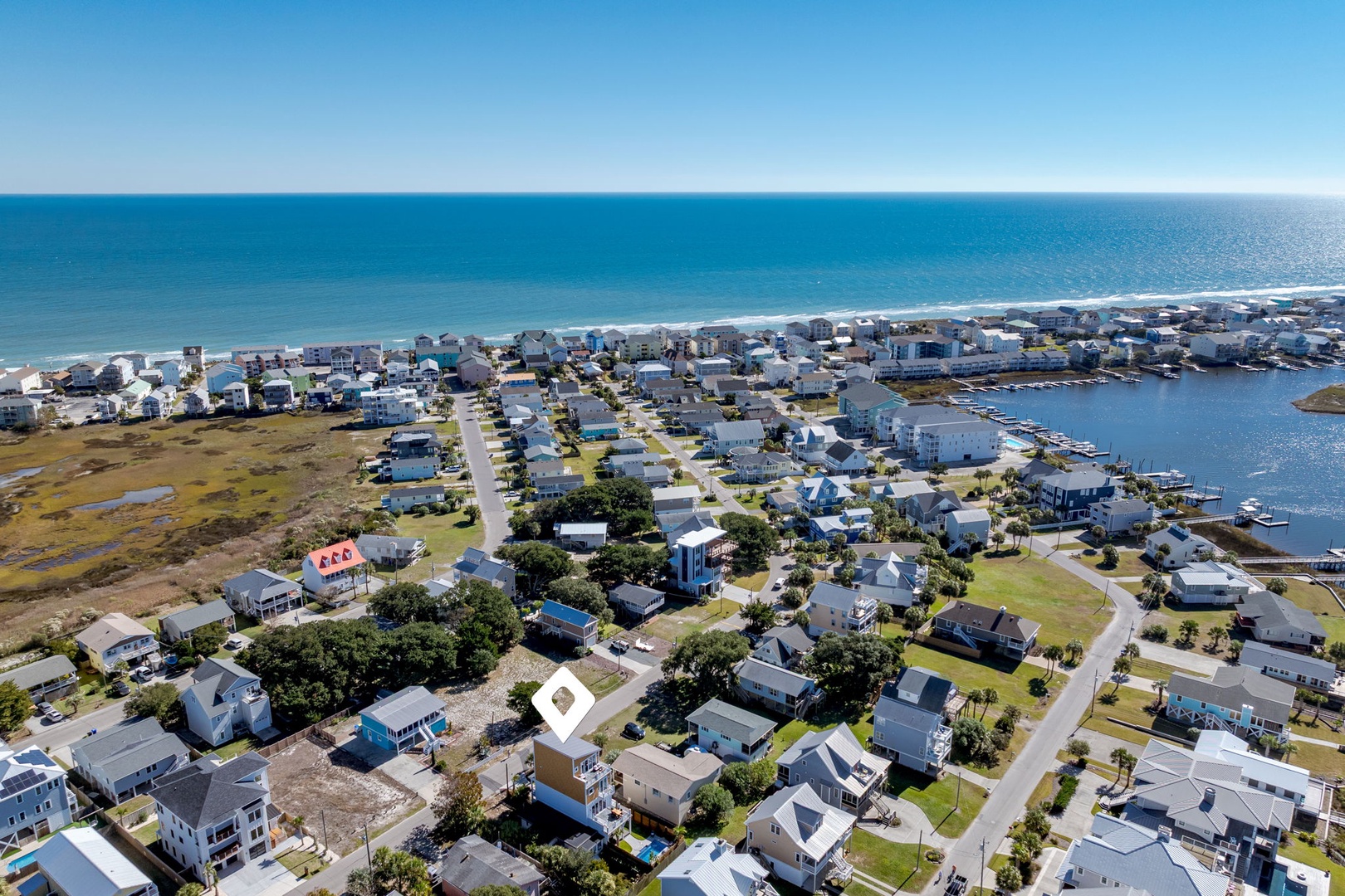 Aerial view of a charming coastal community with beach access and marina, surrounded by pristine waters and sandy shores.