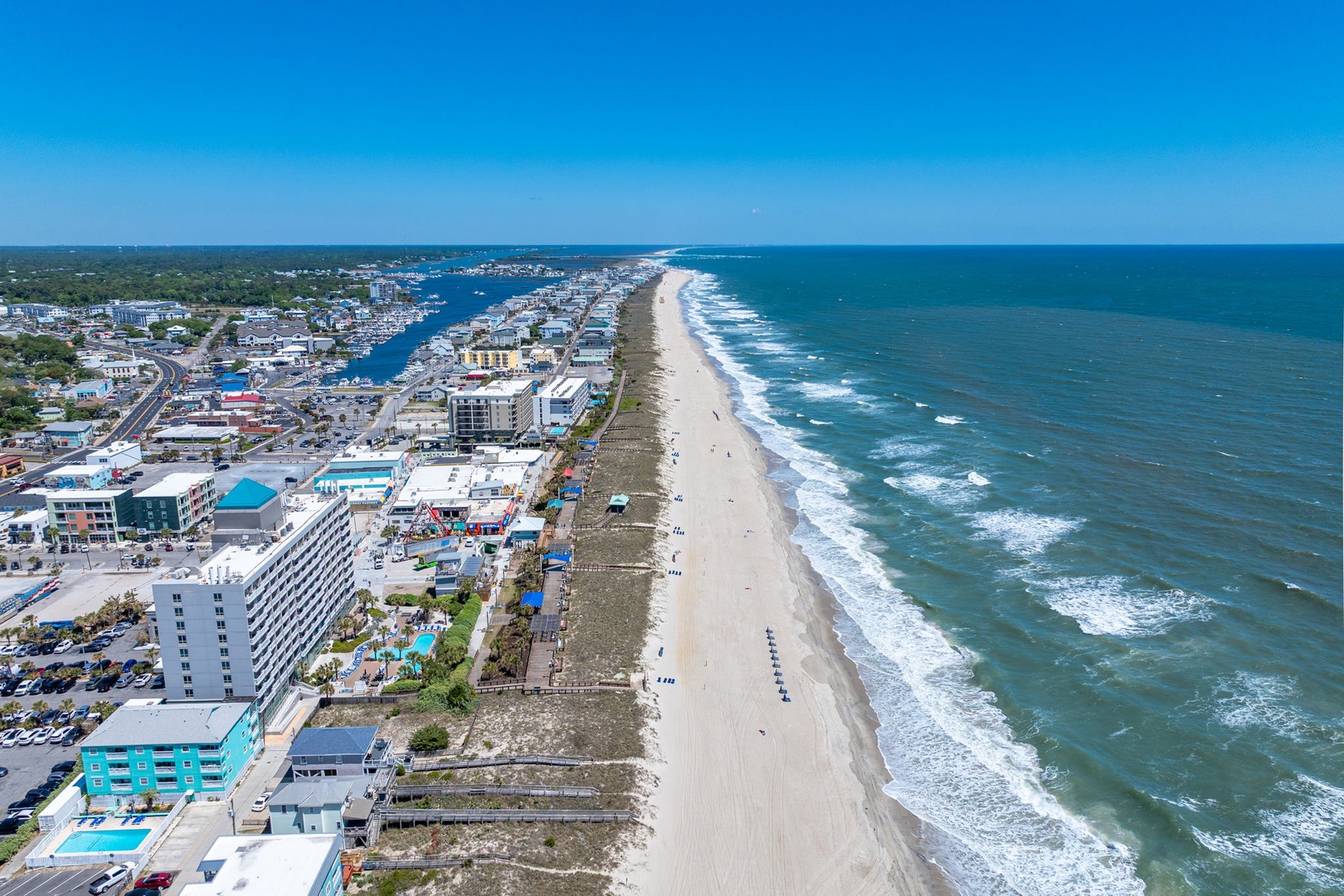 Aerial view of pristine coastline with sandy beach, rolling waves, and waterfront community featuring hotels and residential areas.