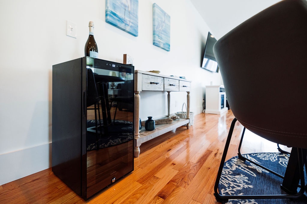 Your own wine fridge awaits, perfectly stocked for intimate evenings on warm hardwood floors beneath serene coastal artwork.