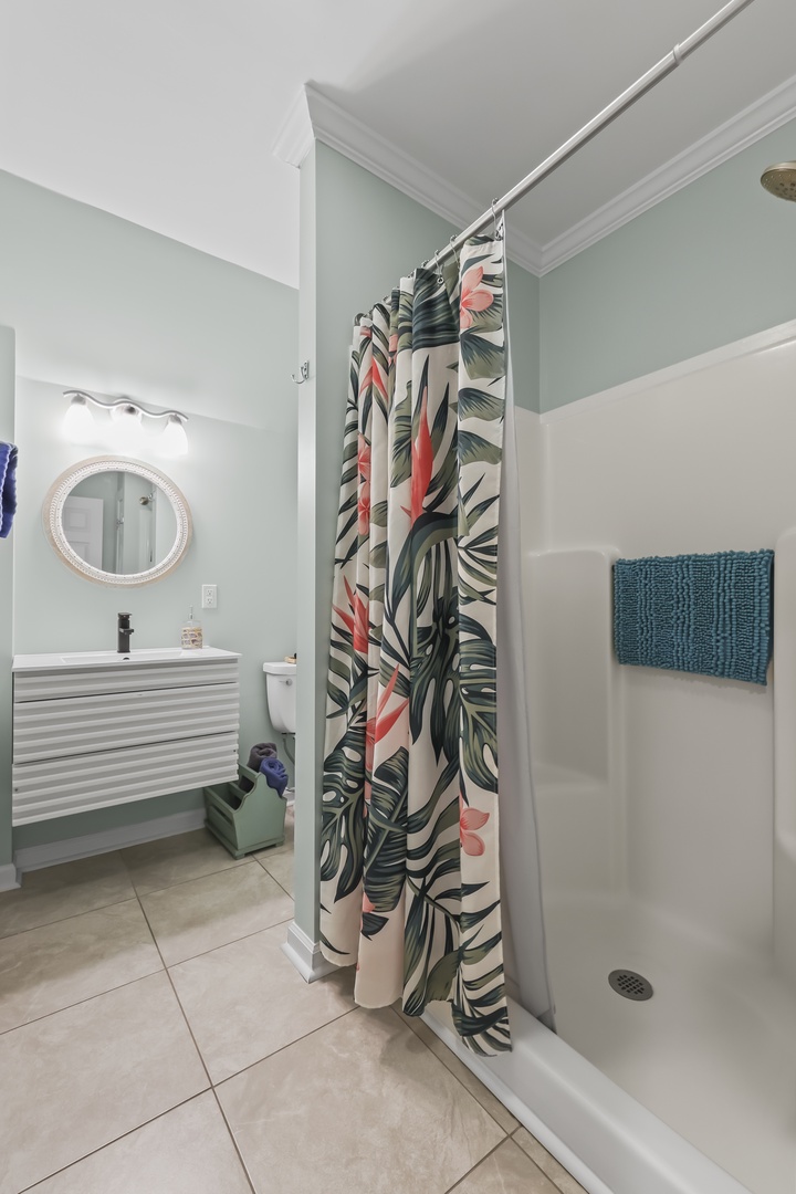 Your private bathroom features a refreshing walk-in shower, modern vanity with elegant round mirror, and tropical-inspired accents for a bright, spa-like retreat.
