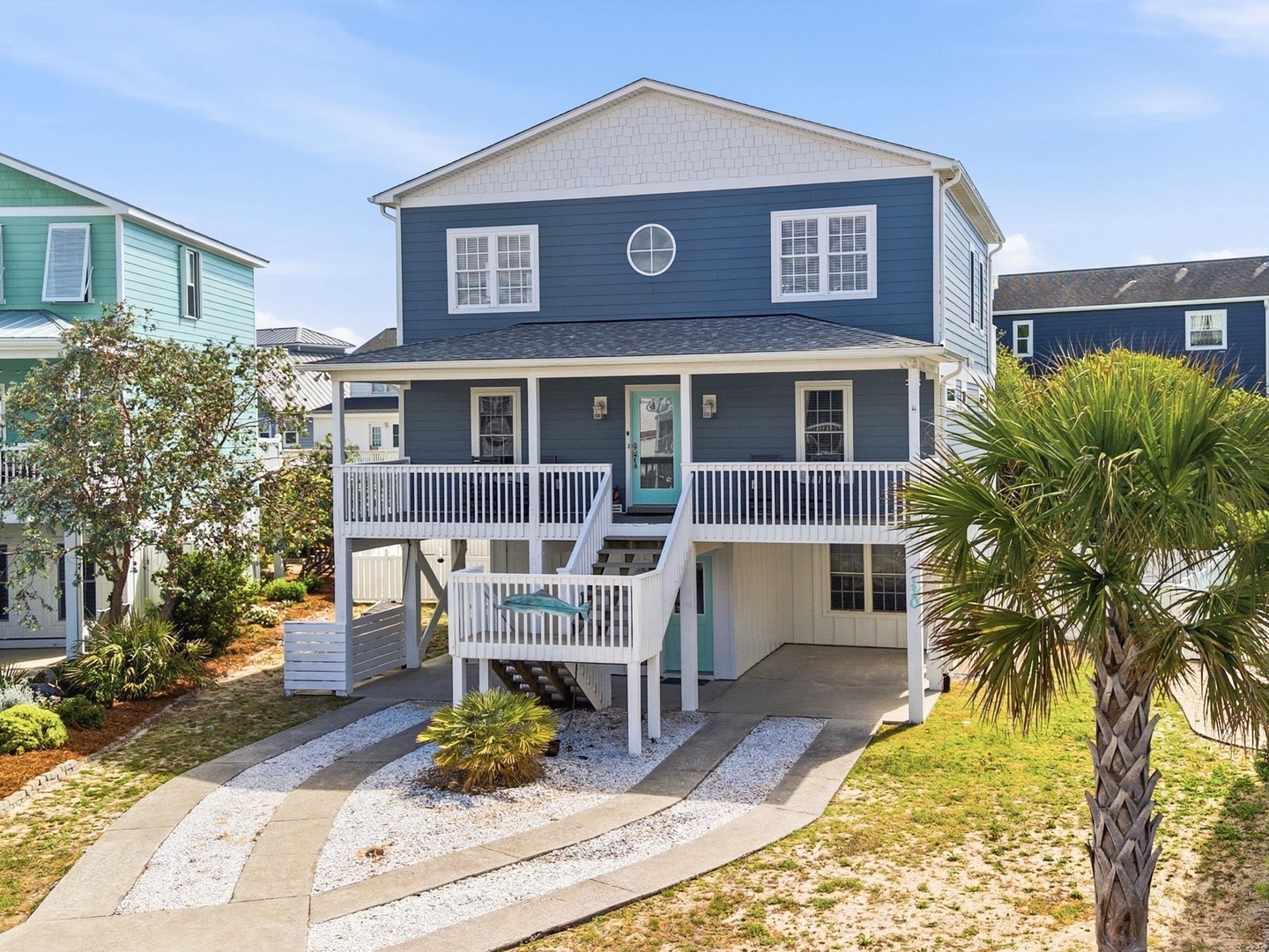 This charming coastal home offers a welcoming front porch and elevated design perfect for beach living. The blue exterior complements the coastal setting, while tropical landscaping and covered parking complete your seaside retreat.