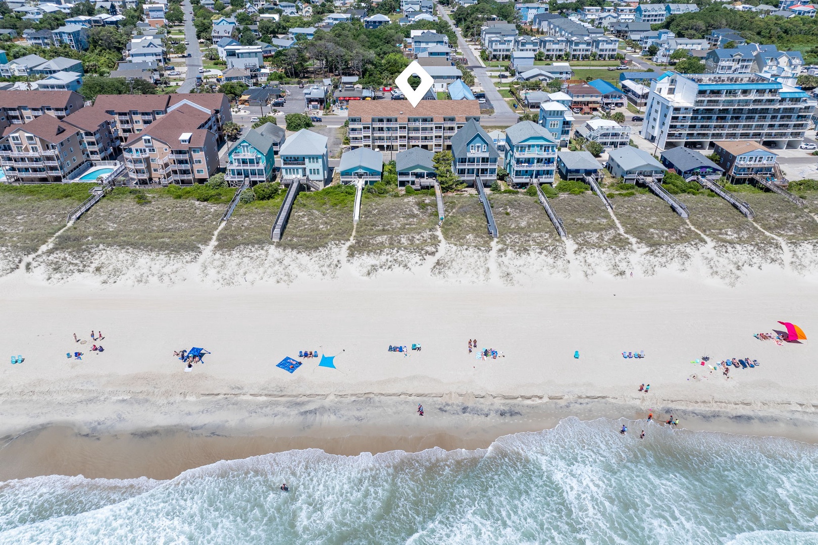 Aerial view of a beachfront vacation rental community with direct beach access, sandy shores, and nearby coastal attractions along a charming residential street lined with beach homes.