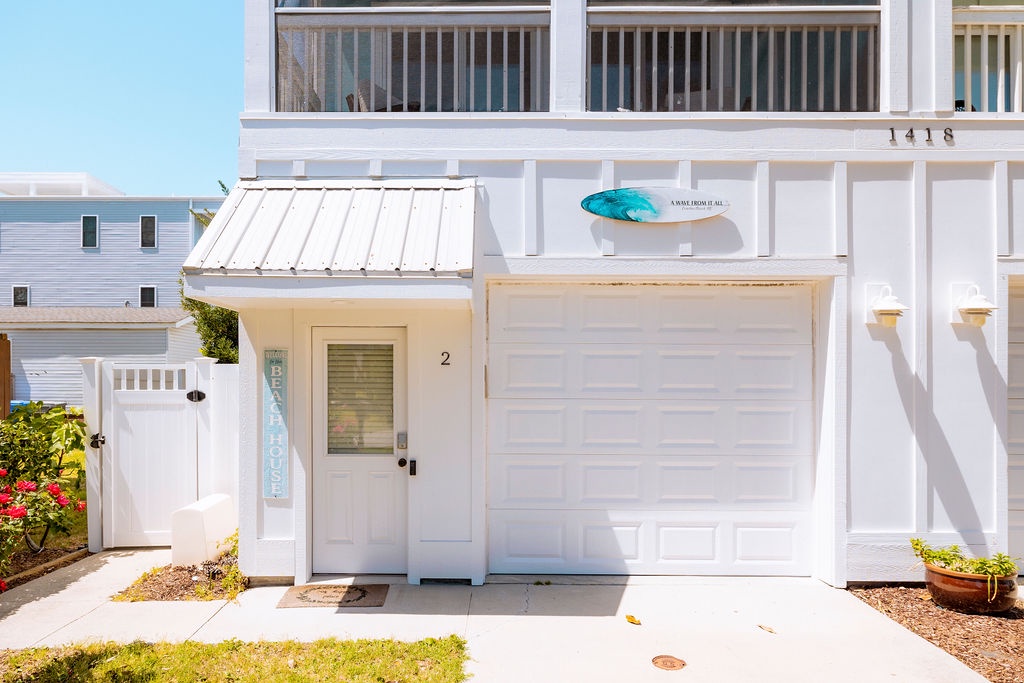 Charming coastal property with bright white exterior, featuring a surfboard decoration and convenient garage parking in a peaceful neighborhood.