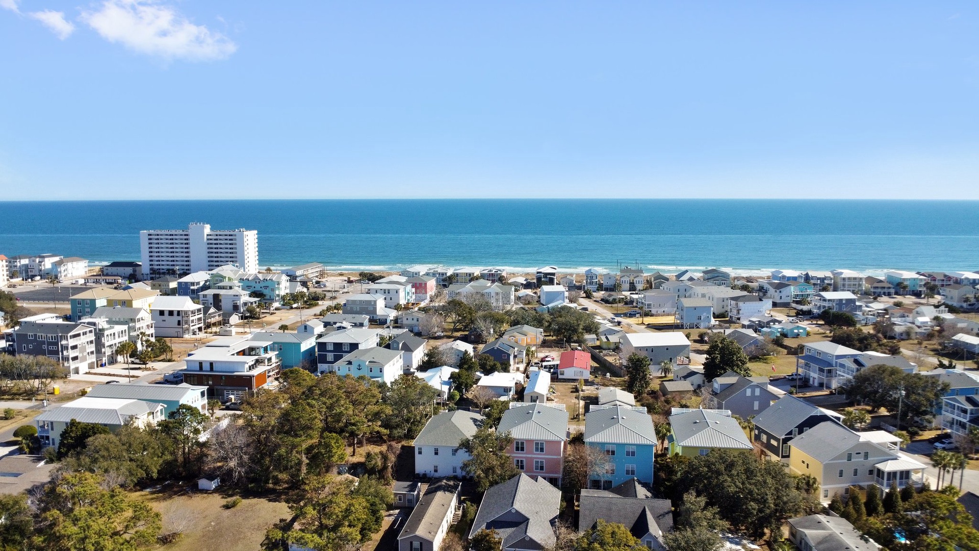 Aerial view of a charming coastal community with colorful homes nestled between lush greenery and pristine oceanfront.