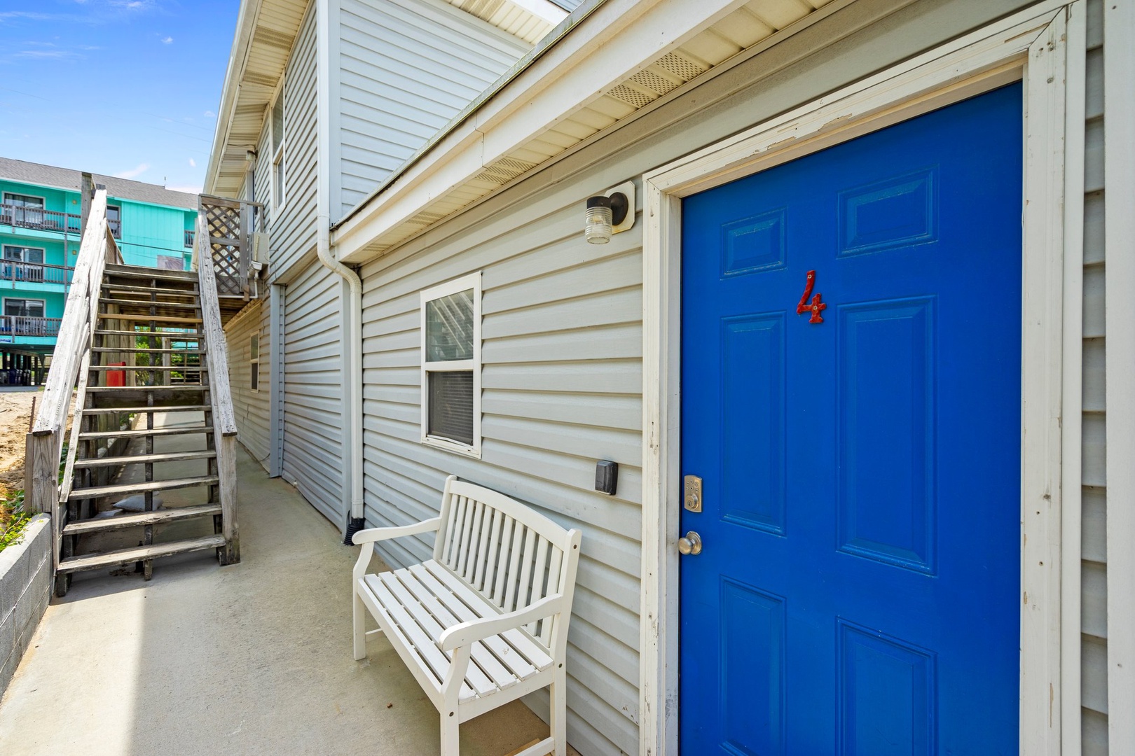Bright blue door welcomes you to your beach getaway. Relax on the covered porch bench before exploring the coastal surroundings.