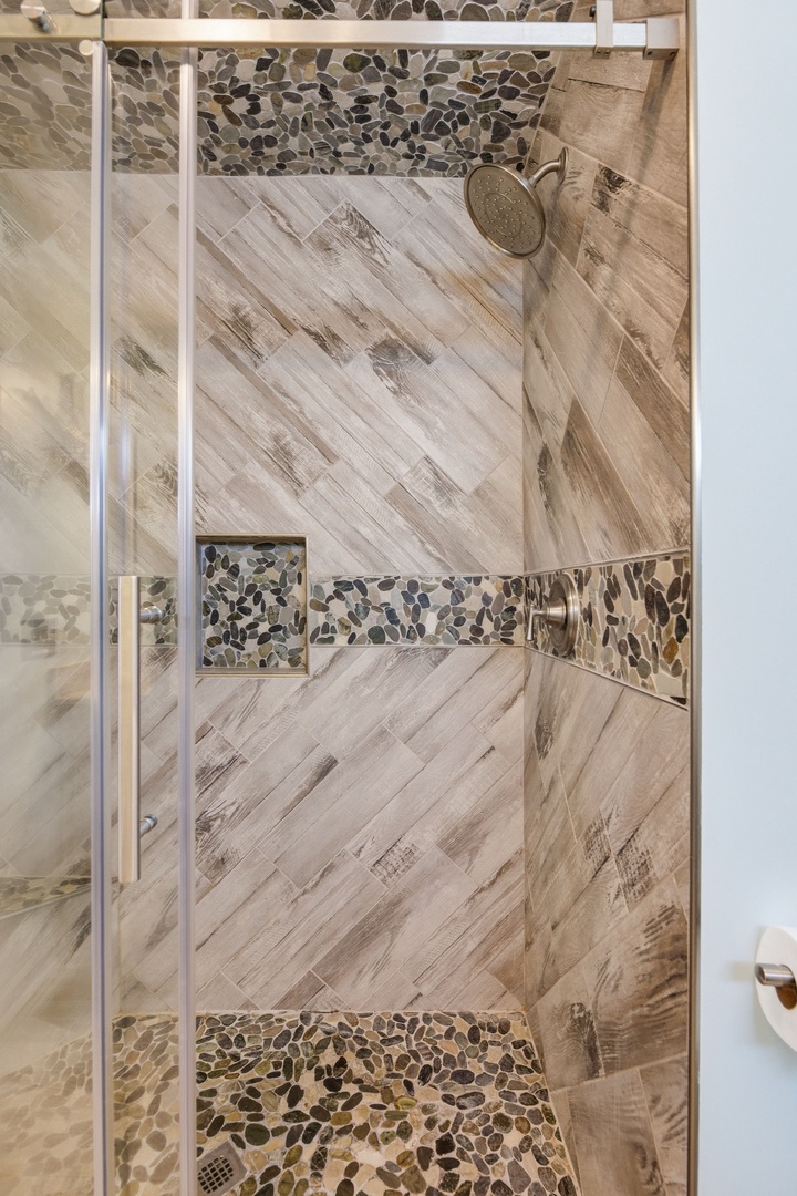 Step into your private spa retreat: a beautifully tiled walk-in shower featuring wood-grain porcelain and elegant river-stone accents that invite relaxation.