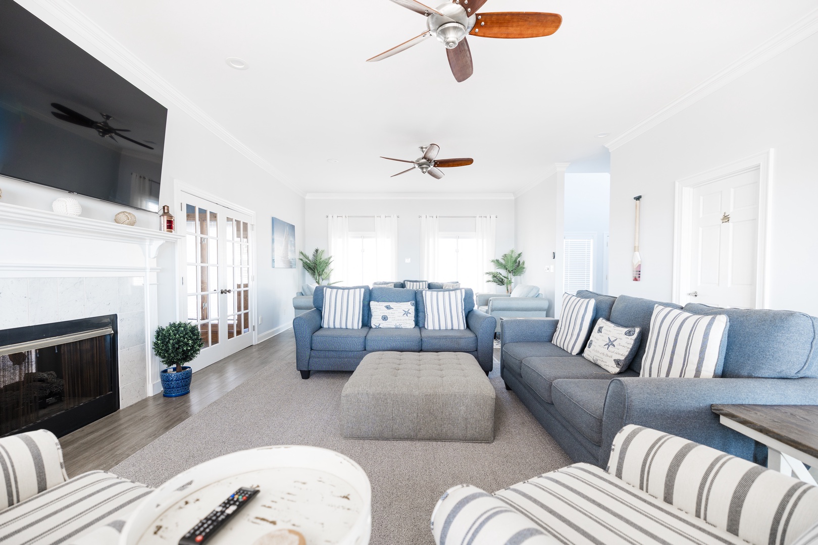 Sink into plush blue sectionals with coastal pillows while ceiling fans keep you cool in this bright, airy living space.