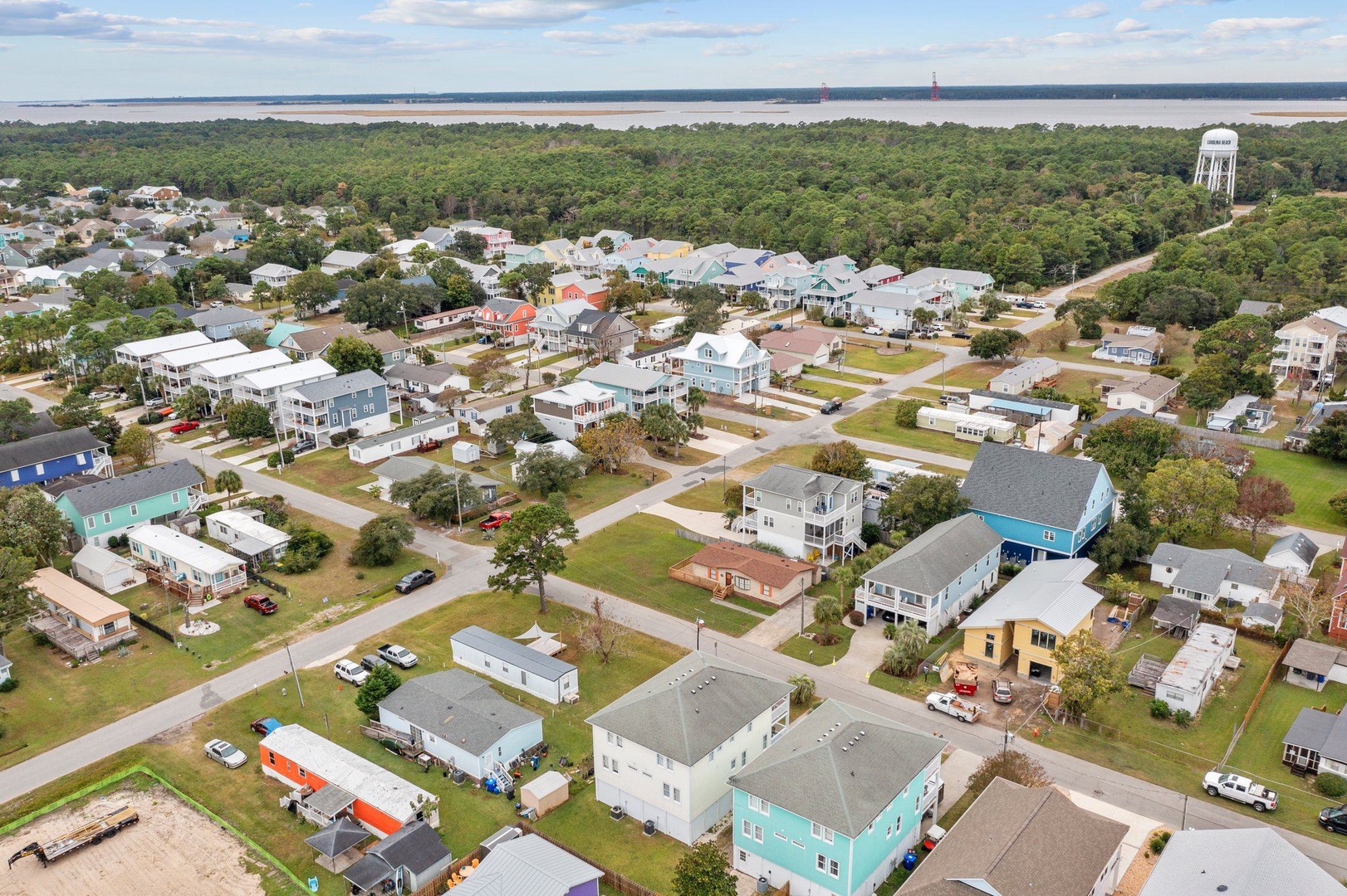 Aerial view of charming coastal neighborhood with colorful homes nestled between lush forests and sparkling waterfront.