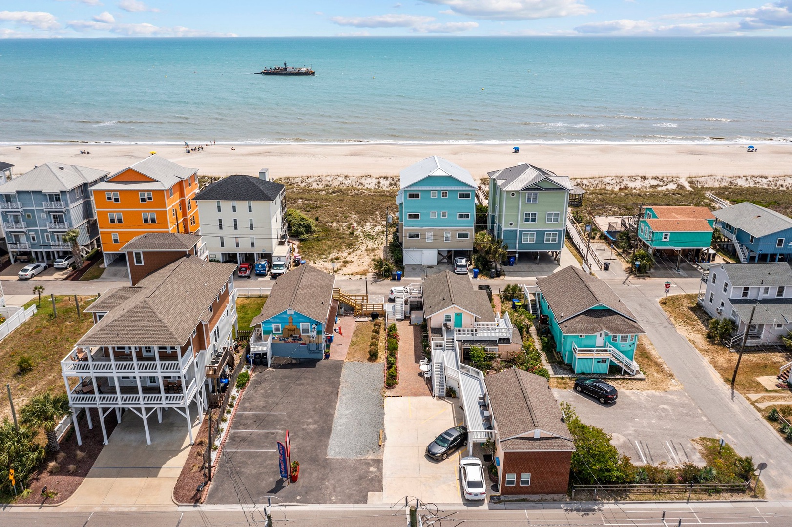Colorful beachfront vacation homes line the sandy shore, offering direct beach access and stunning ocean views with a boat visible offshore.