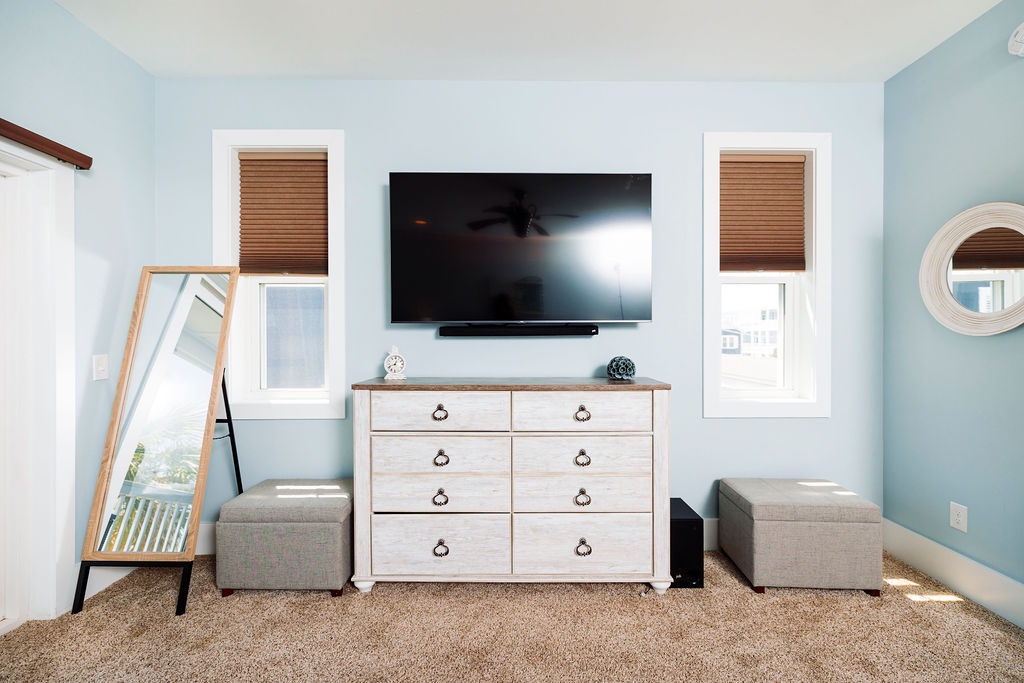 Relax in your serene bedroom sanctuary with calming blue walls, entertainment center, and cozy storage ottomans for ultimate comfort.