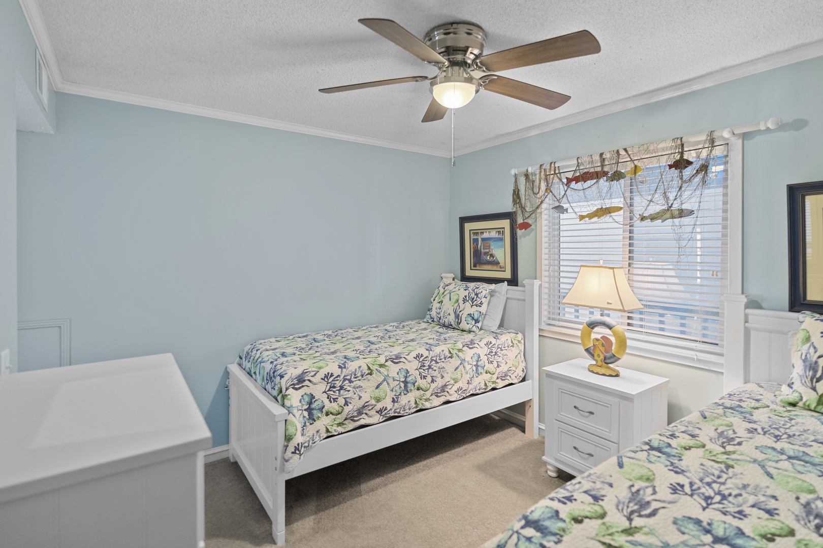 Your coastal-themed bedroom features twin beds with tropical linens and nautical decor, perfect for a refreshing seaside escape.