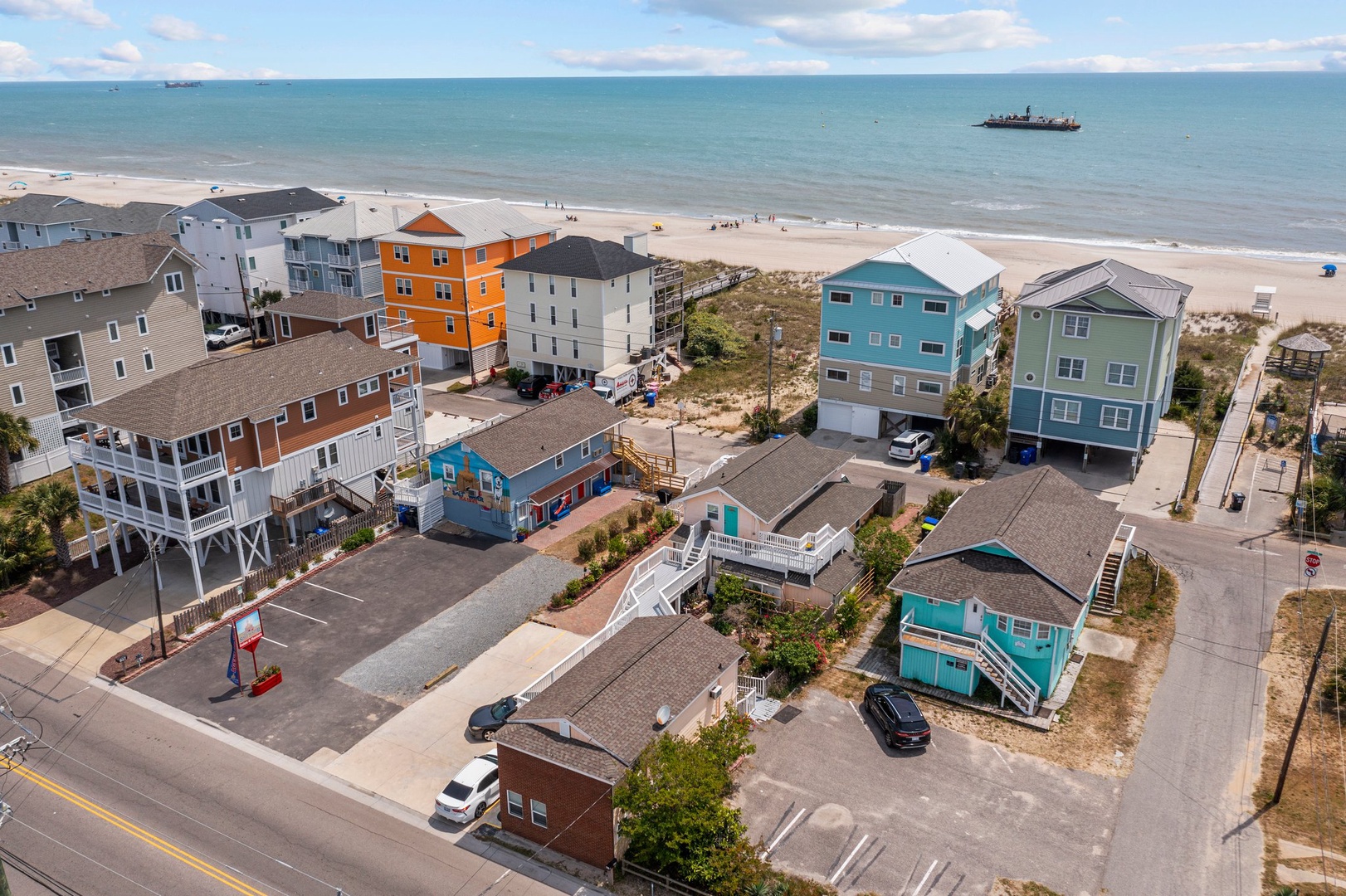 Colorful beachfront vacation rentals line the sandy shore, offering prime oceanfront access with convenient parking and nearby amenities for the perfect coastal getaway.