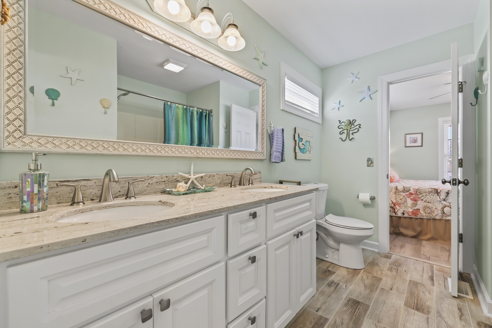 Freshen up in your coastal-inspired bathroom with soft seafoam walls, beach-themed decor, granite dual vanities, and elegant lighting that creates a serene, spa-like retreat.