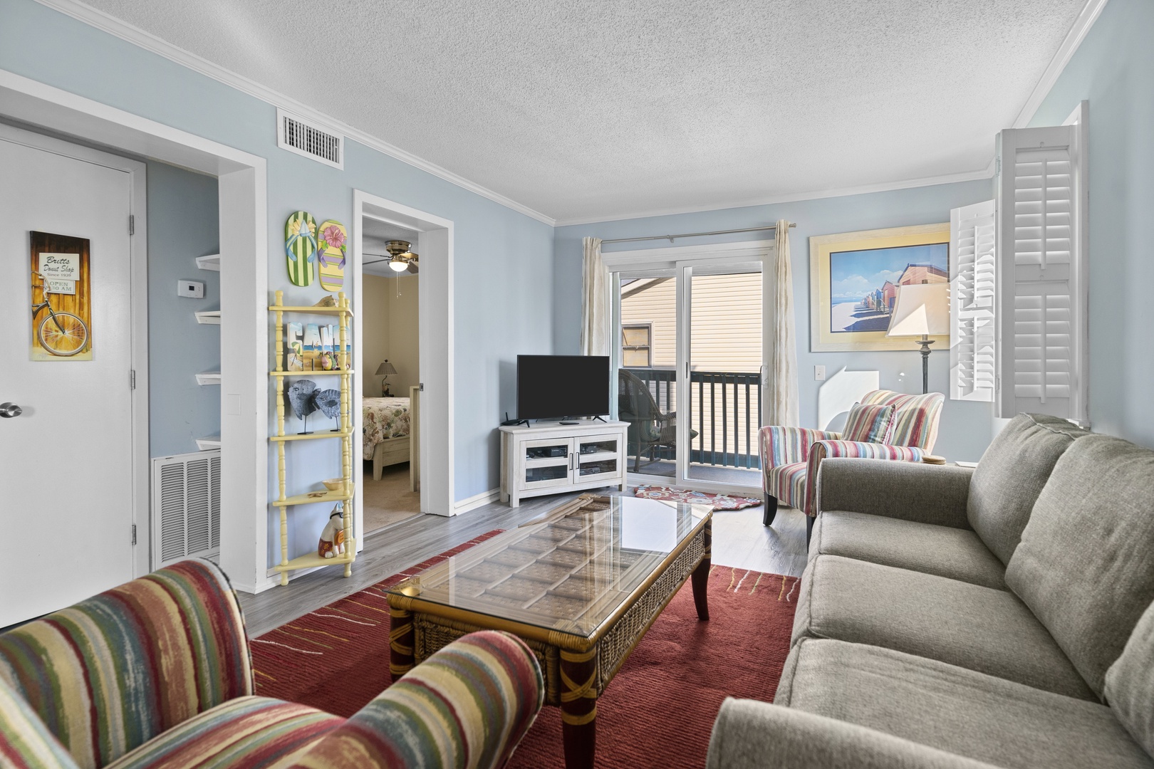 Relax in your coastal-themed living room with plush seating, modern entertainment center, and balcony access for afternoon breezes.