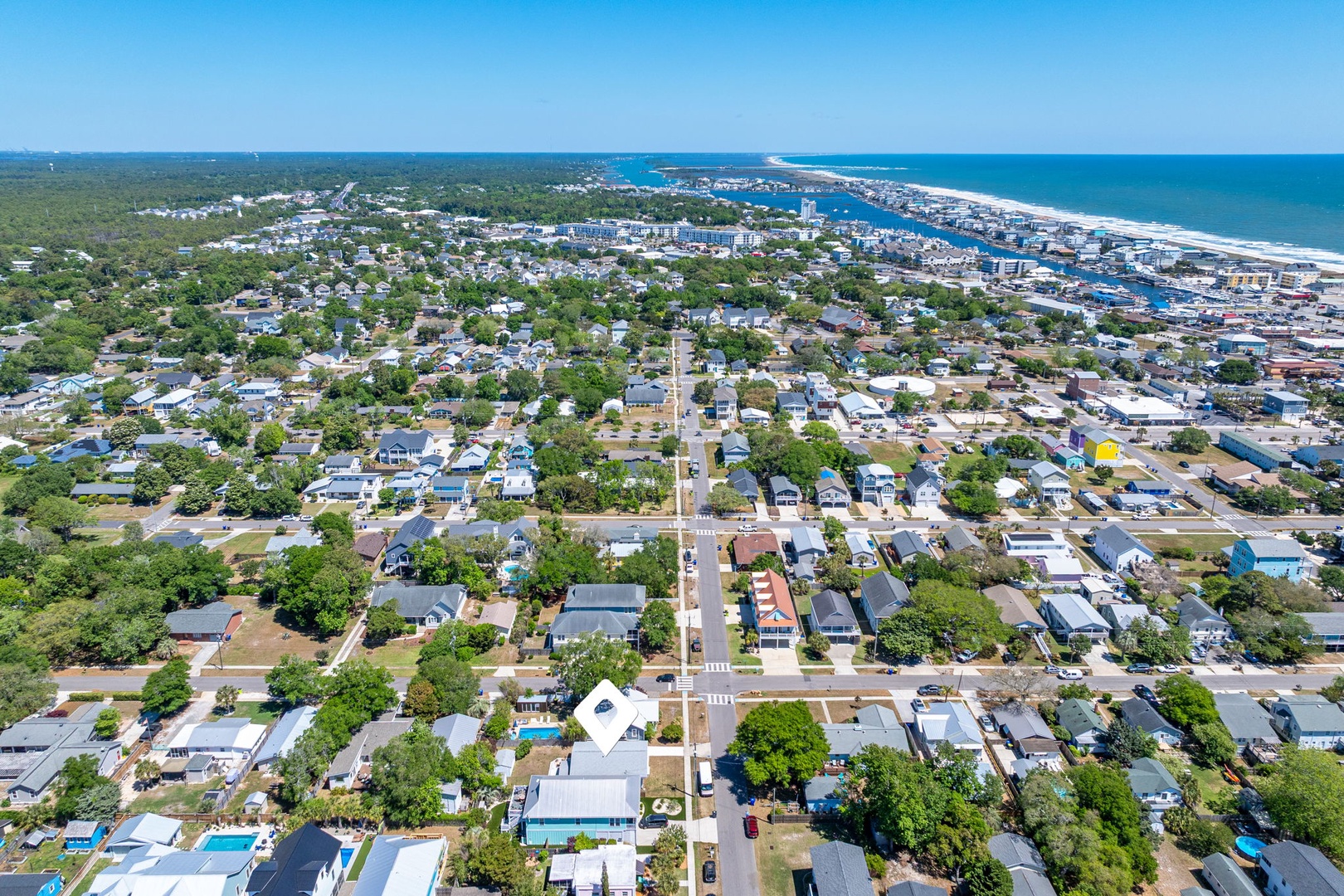 Aerial view of a charming coastal town with tree-lined streets leading toward pristine beaches and sparkling ocean waters.