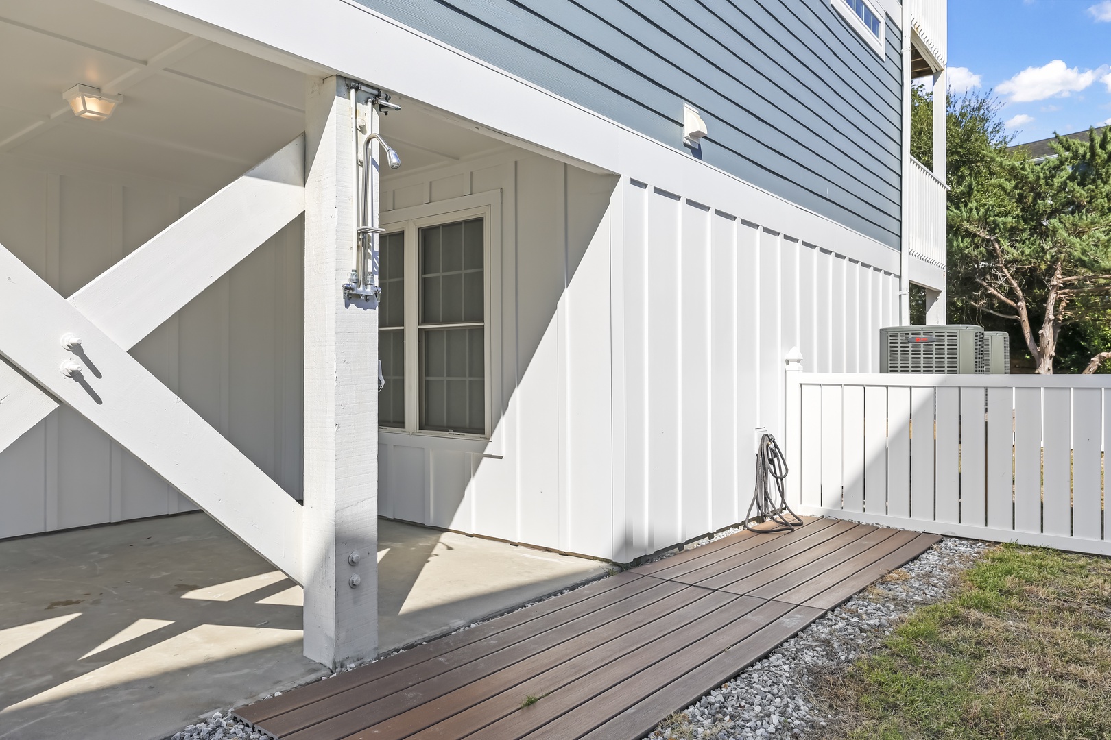 The exterior features clean white siding and a private fenced patio area with an outdoor shower—perfect for rinsing off after a day at the beach.