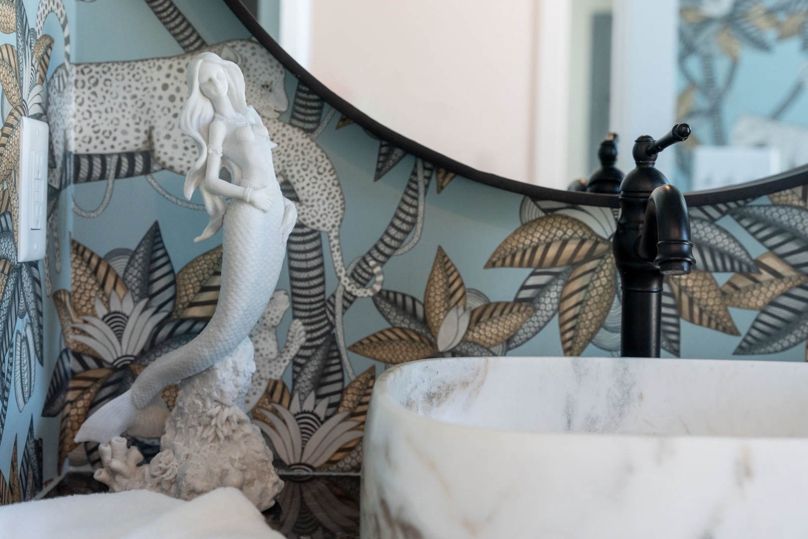 Your bathroom features tropical wallpaper, marble vessel sink, oil-rubbed bronze faucet, and charming mermaid décor creating a whimsical coastal retreat.