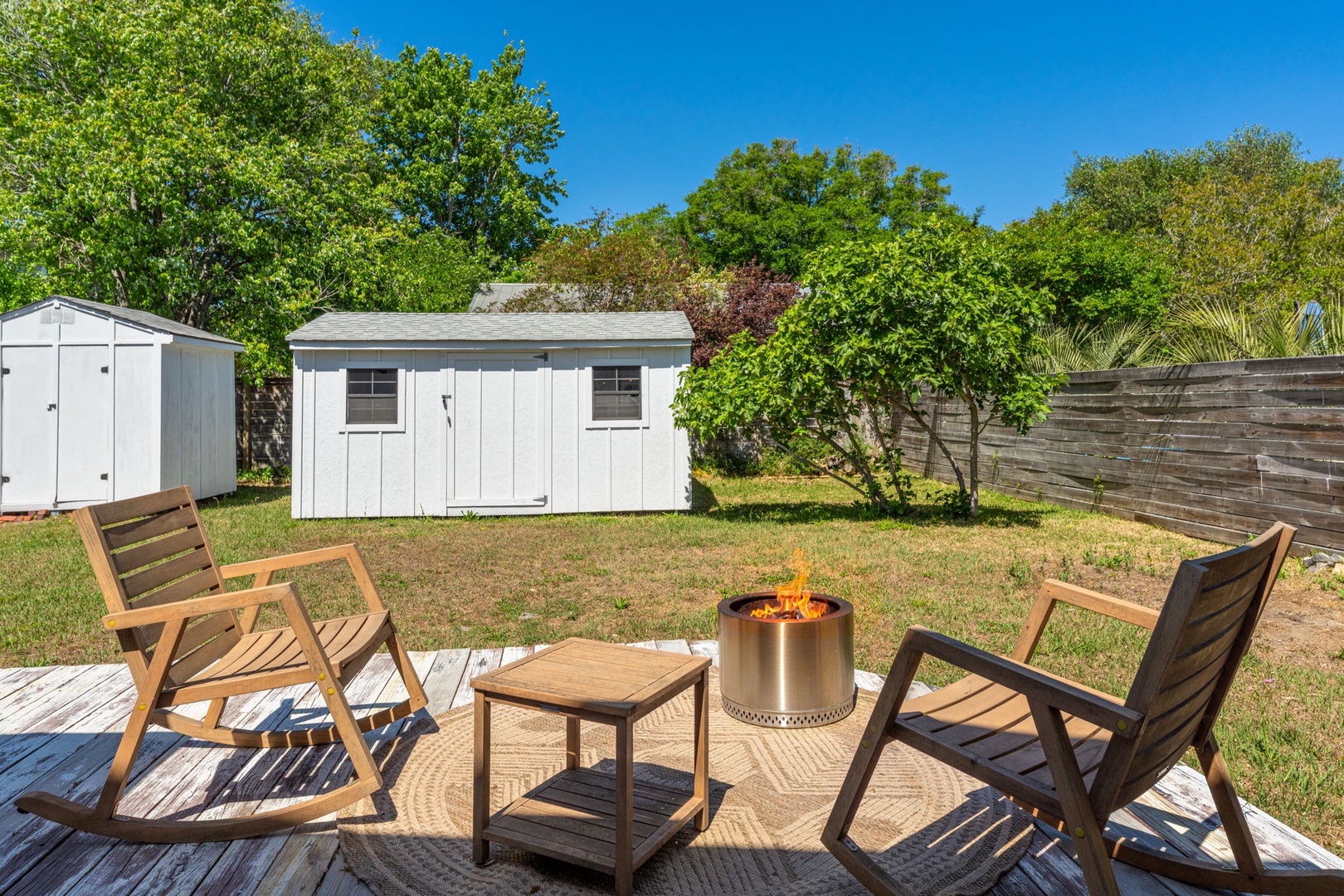 Gather around your private fire pit on the wooden deck, surrounded by lush greenery and peaceful backyard views.