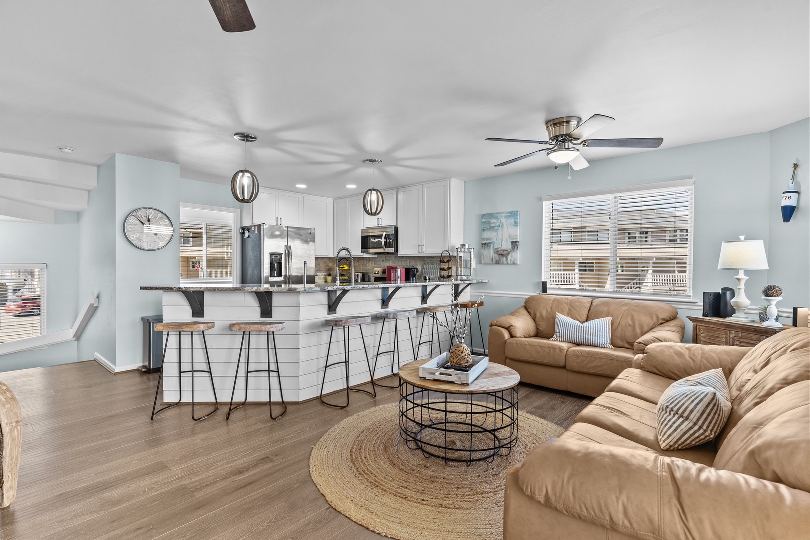 Relax in your open-concept living space where coastal blues meet warm leather seating, perfect for gathering around the stylish coffee table.