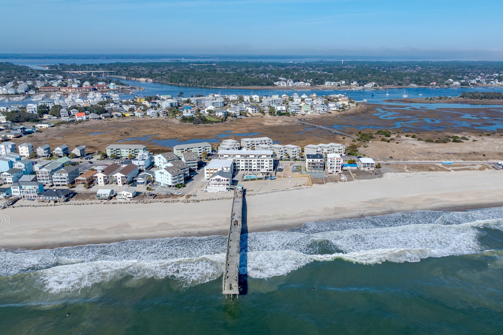 Aerial view of a coastal vacation destination with beachfront properties, sandy shores, and a fishing pier extending into turquoise waters.
