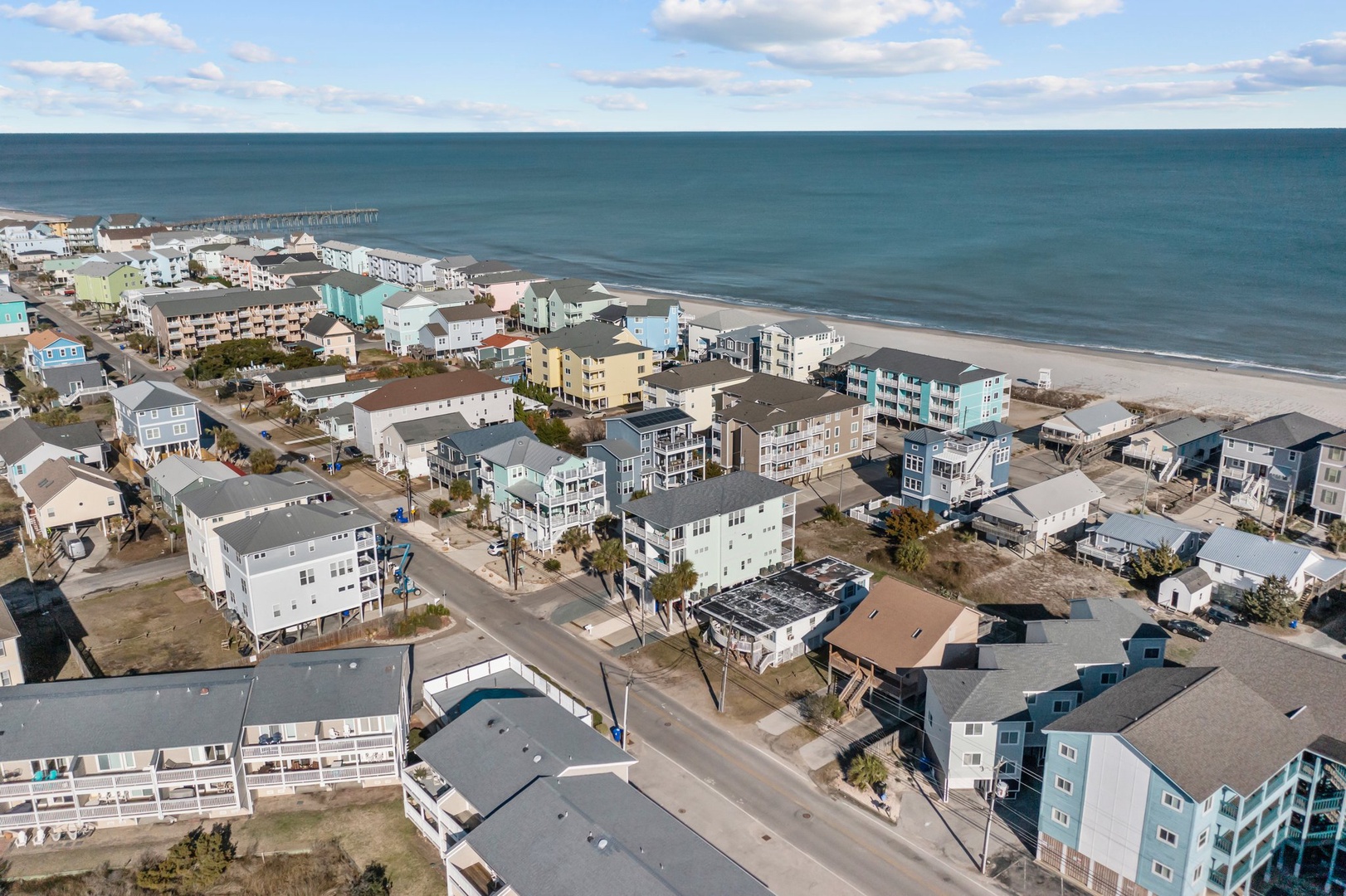 Aerial view of a charming beachfront community with colorful vacation homes stretching along pristine sandy shores and turquoise waters.