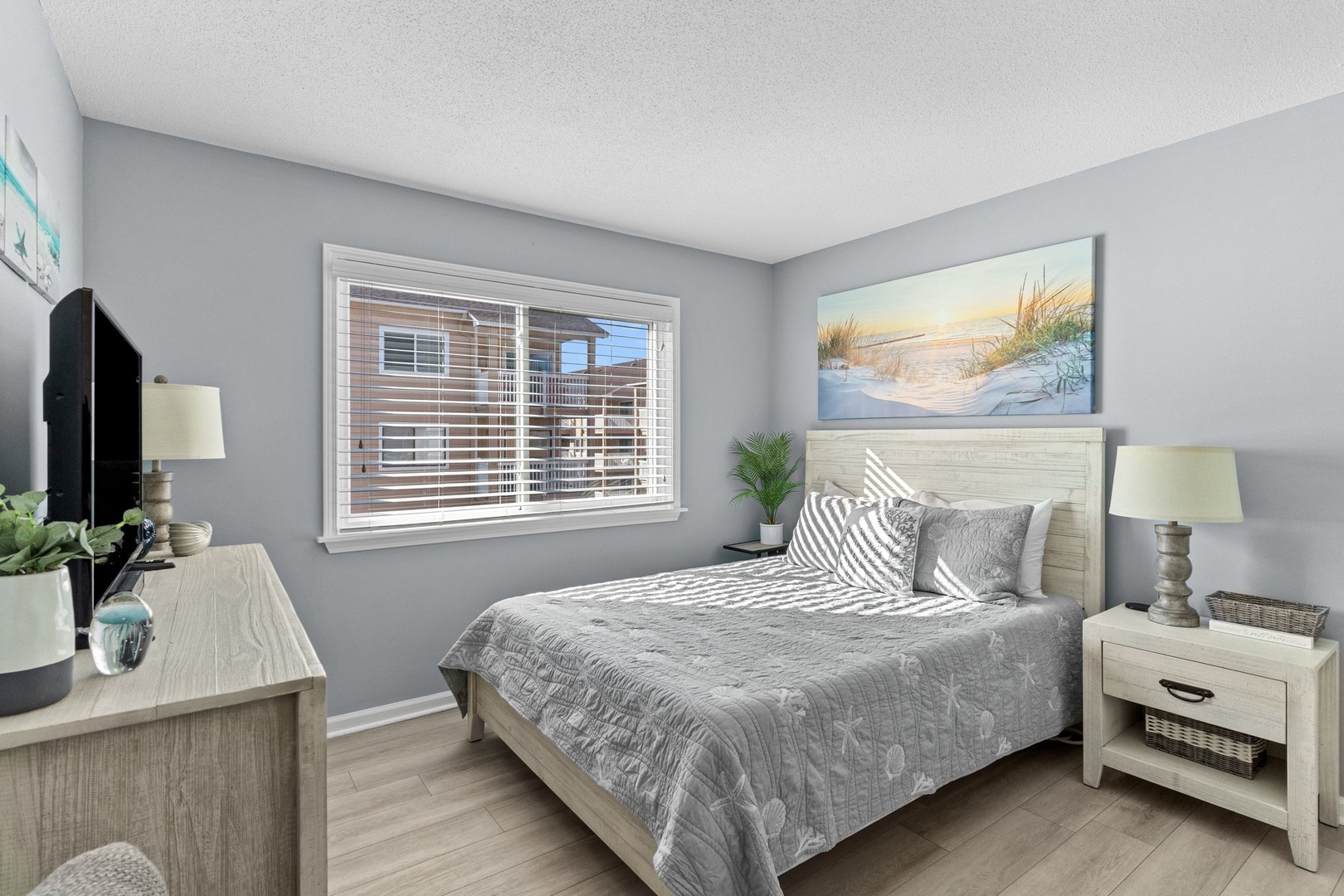 Drift off to sleep in your serene coastal bedroom, where soft grays meet beach-inspired artwork and modern comfort.