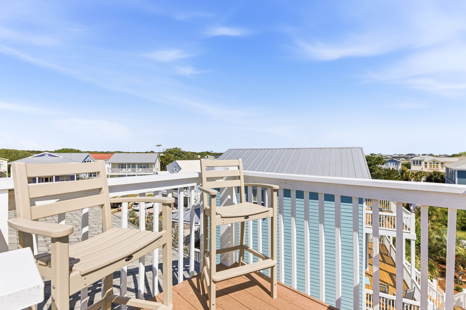 A coastal neighborhood with beach cottages and lush greenery stretches across the horizon under a clear blue sky, marking the peaceful surroundings of this property.