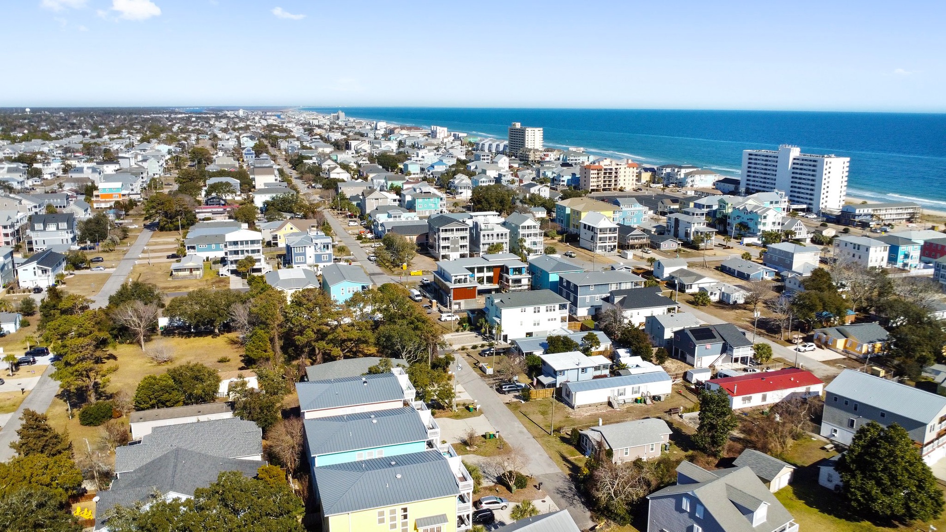 Aerial view of a charming coastal town with residential neighborhoods stretching toward pristine beaches and ocean waters.