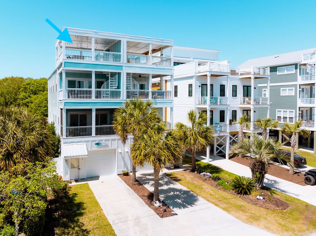 Coastal vacation home with multiple levels, white exterior, turquoise accents, and palm tree landscaping in a sunny beach community.