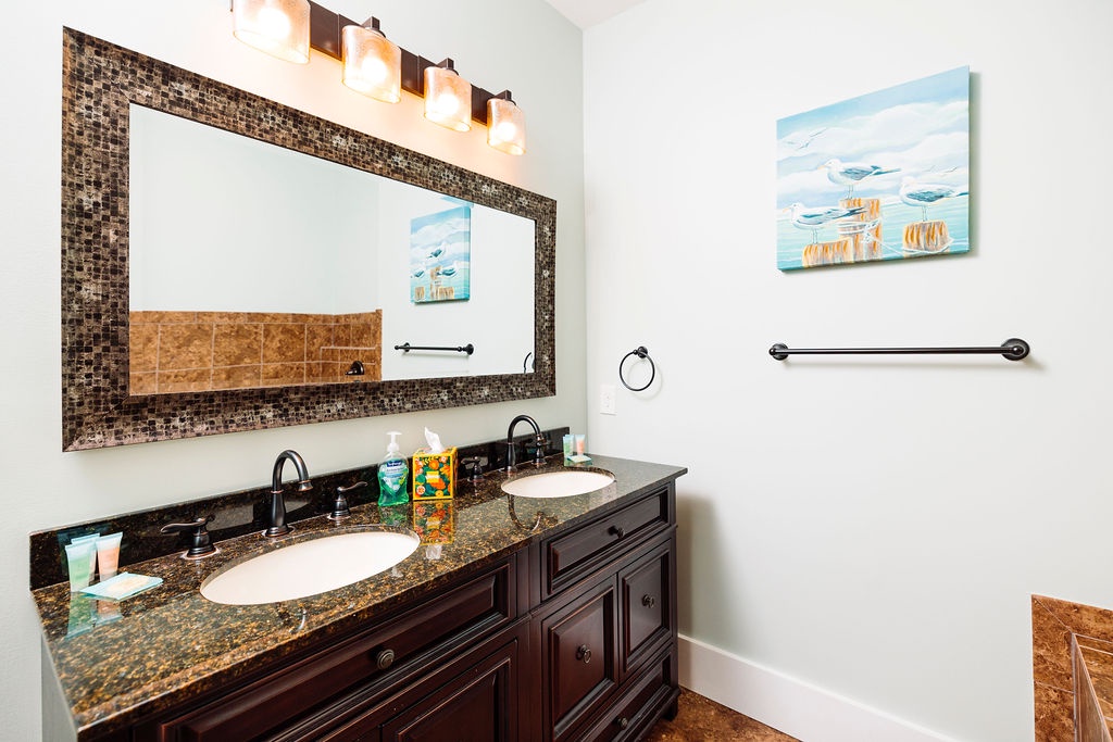 Refresh in your elegant dual-sink bathroom with granite countertops, mosaic mirror frame, and warm lighting that creates the perfect spa-like ambiance.