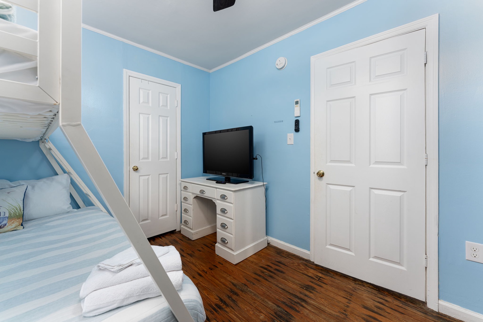 A serene coastal-colored bedroom with bunk beds and a charming white desk, perfect for relaxing after your beach adventures. Enjoy entertainment on the flat-screen TV.