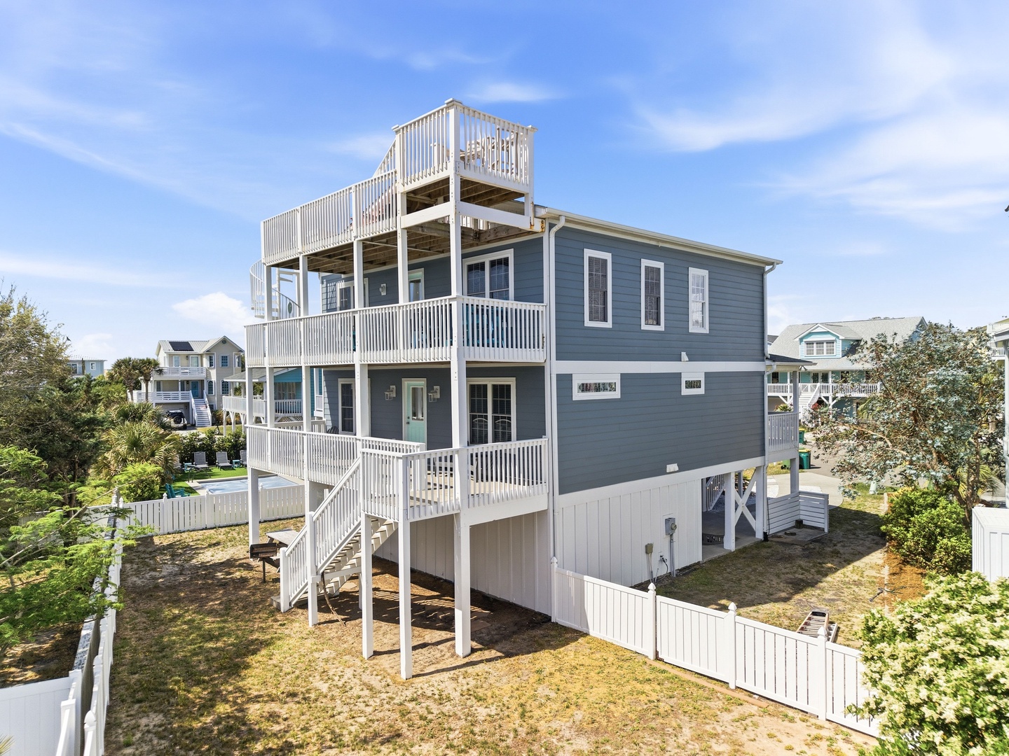 Coastal property featuring multi-level deck spaces and rooftop observation deck, situated in a quiet residential neighborhood near the beach with neighboring homes visible in the background.