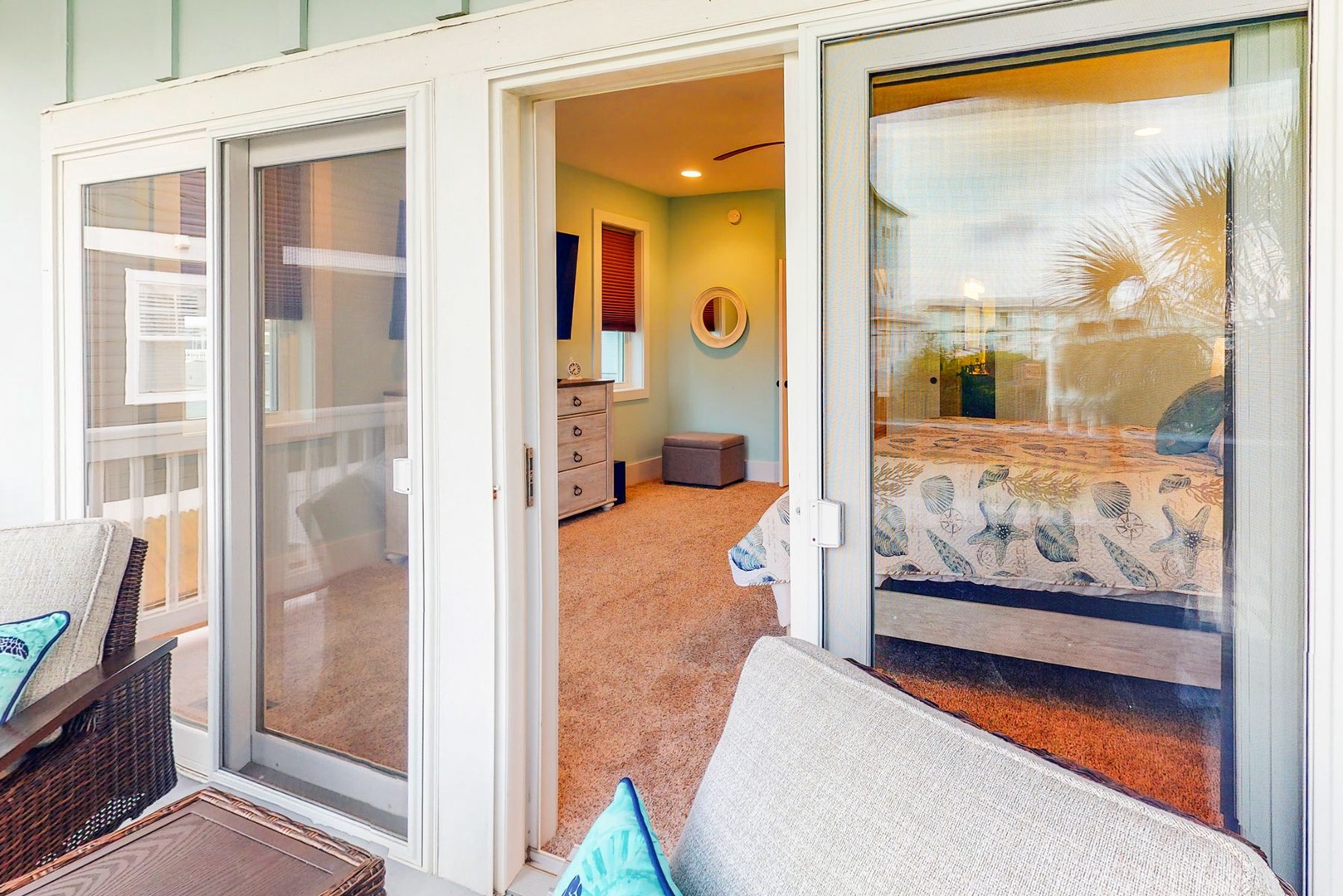 Step into your bright bedroom through sliding glass doors, where coastal-themed bedding and warm lighting create your perfect retreat.