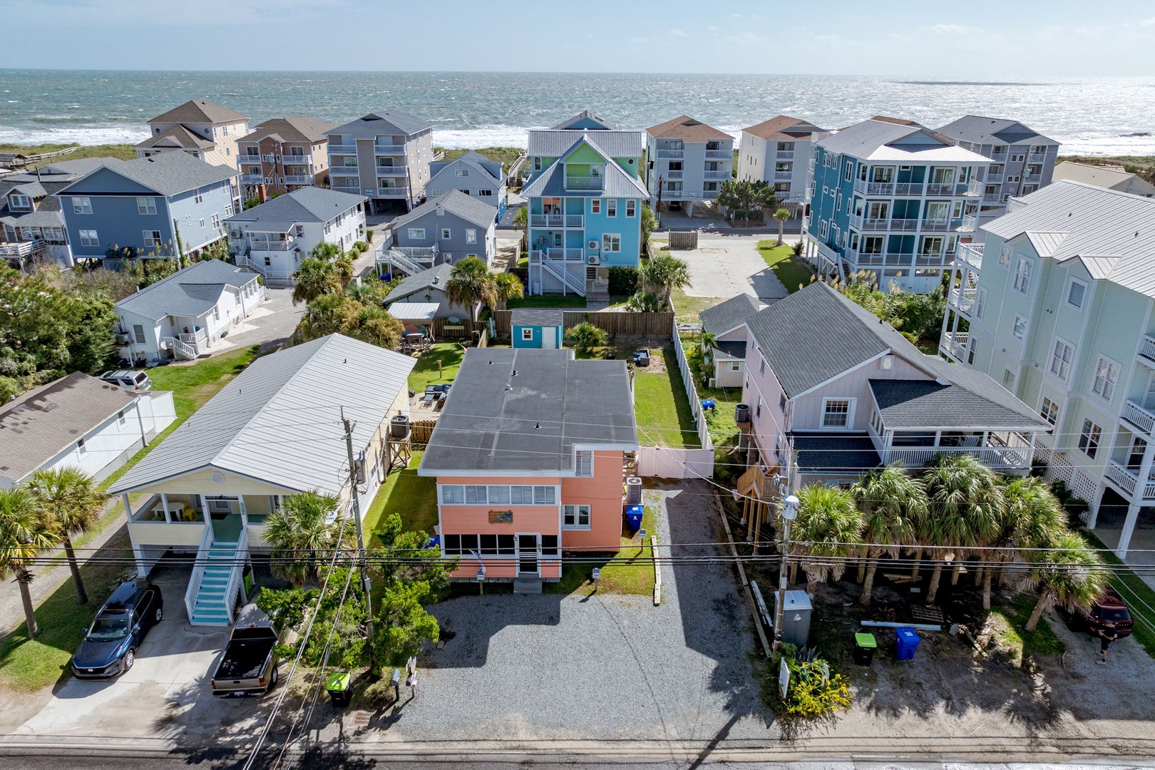 Aerial view of colorful beachfront vacation homes nestled between the ocean and residential neighborhood, showcasing the coastal community setting.
