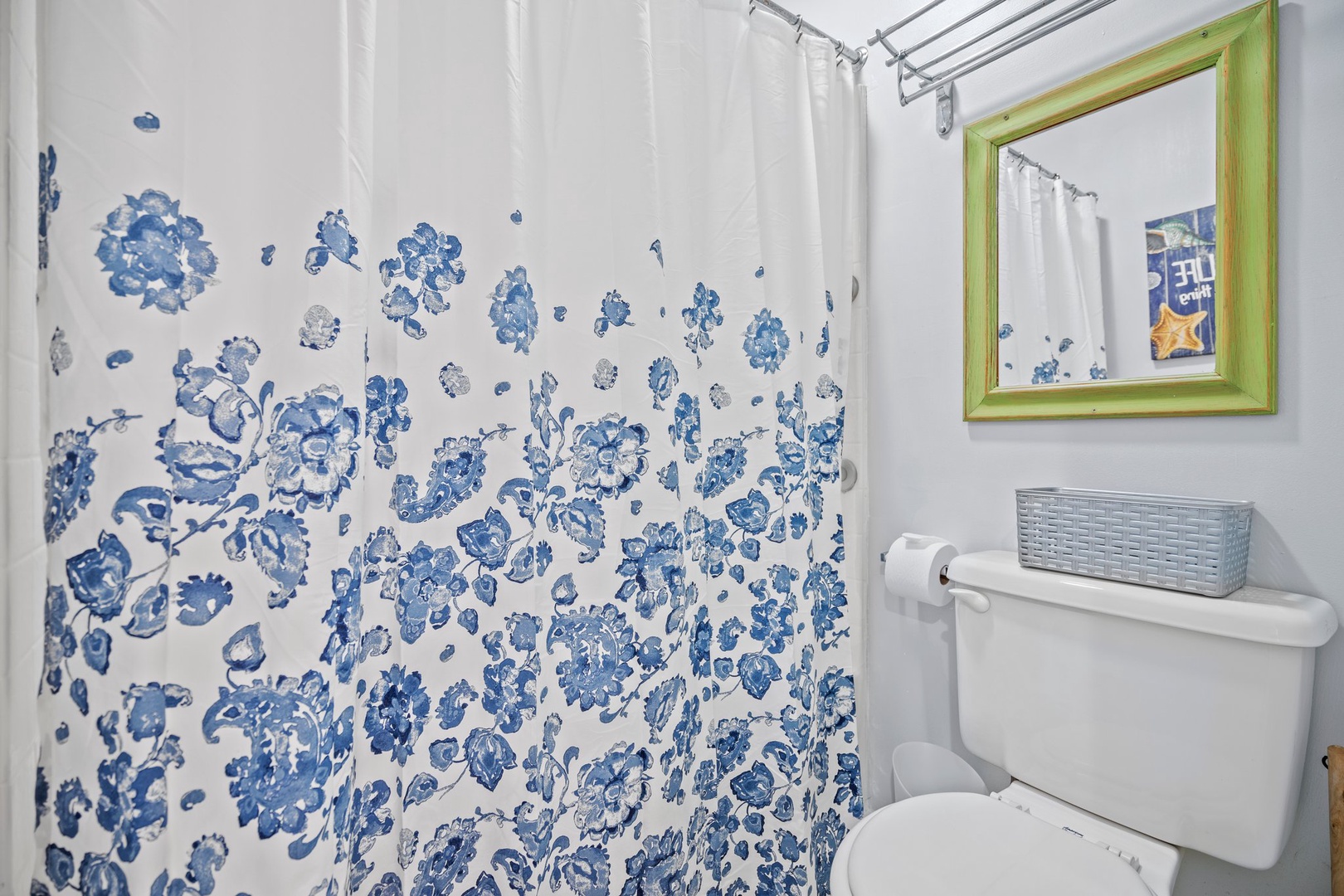 Step into your bright, cheerful bathroom with charming blue floral shower curtain and green-framed mirror adding personality to your private retreat.