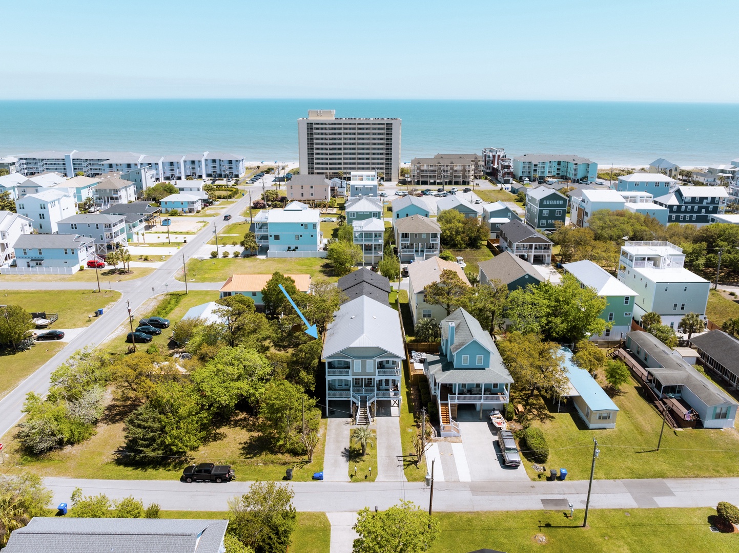 Aerial view of beachfront neighborhood with vacation rental homes nestled among mature trees, just steps from the ocean.