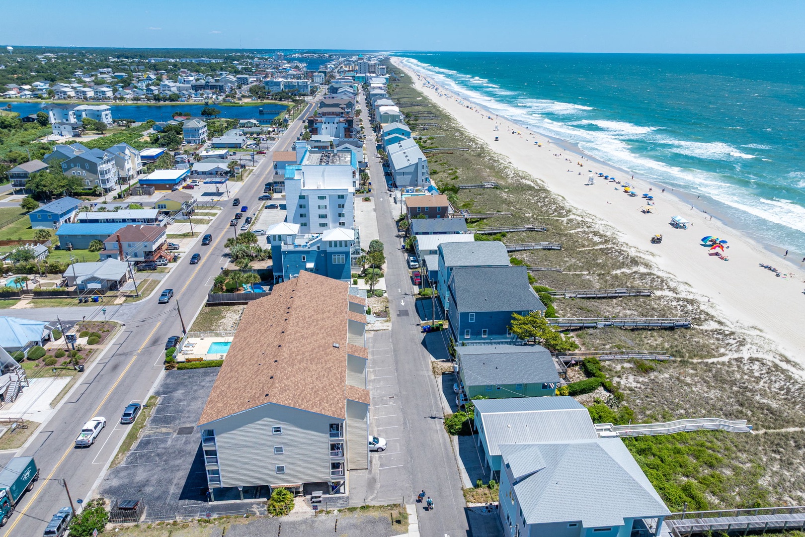 Aerial view of a beachfront coastal community featuring vacation rental properties along a pristine white-sand beach with rolling turquoise waves and residential streets.
