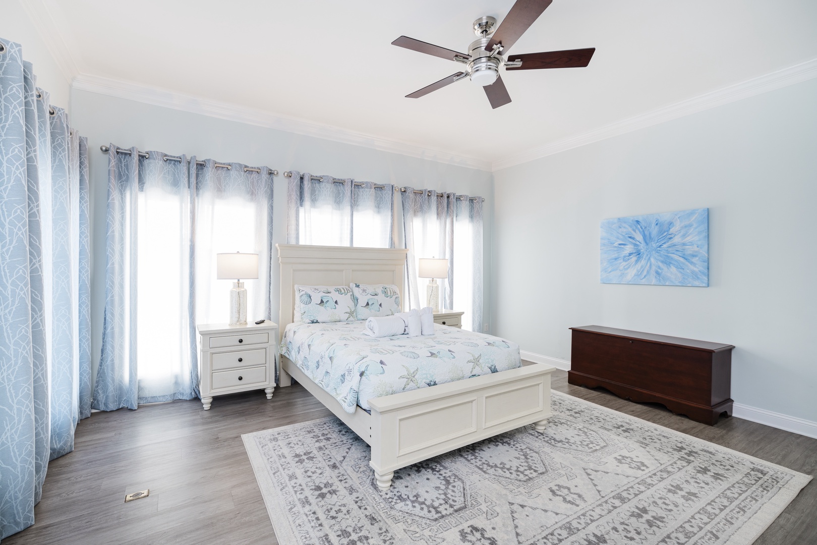 Relax in your serene bedroom with soft blue coastal linens and gentle ceiling fan breeze for peaceful nights.