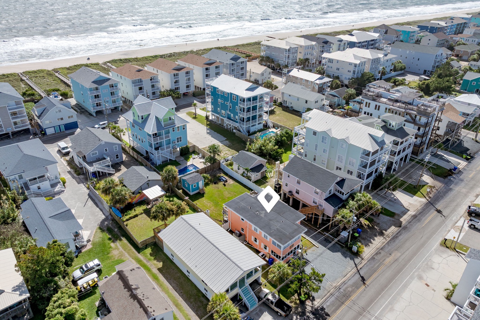 Aerial view of a charming beachfront community featuring colorful coastal homes and vacation rentals just steps from the sandy shore.