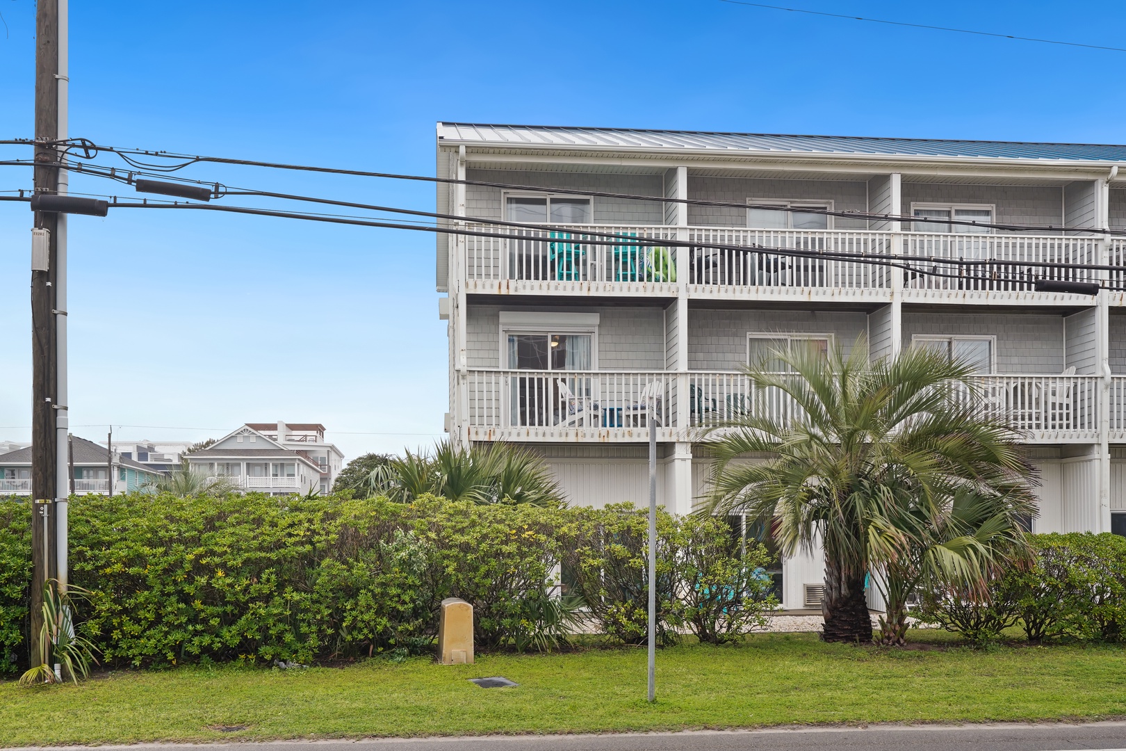 Modern beachside building featuring multiple levels with private balconies, surrounded by lush tropical landscaping and palm trees.