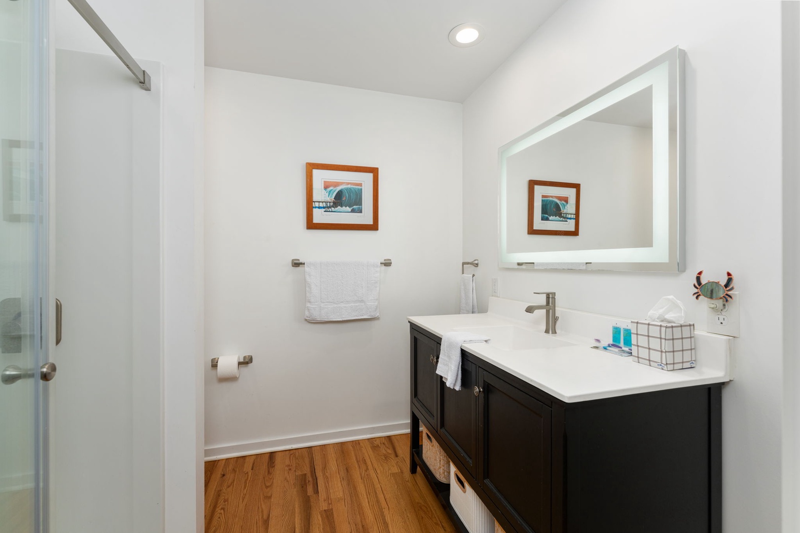 Step into your serene bathroom sanctuary with elegant dark vanity, illuminated mirror, and premium amenities thoughtfully arranged for your comfort.