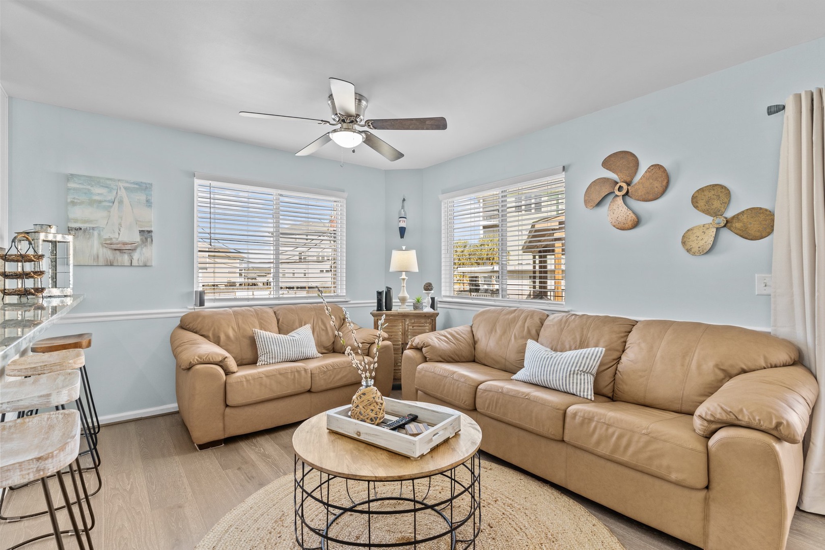 Sink into plush leather sofas beneath nautical propeller art in your coastal living room, where ceiling fans keep you cool.