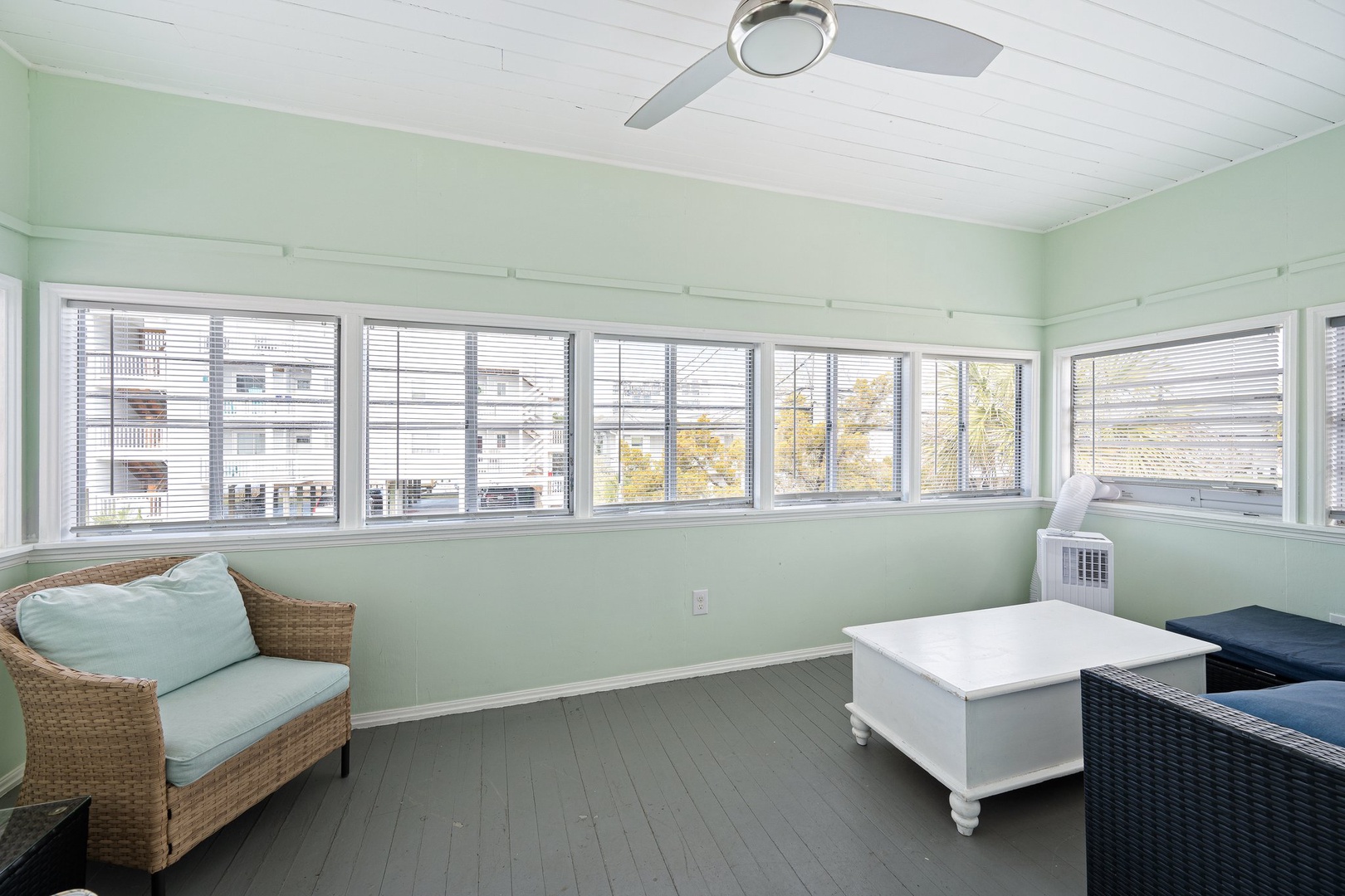 Relax in your bright sunroom with panoramic windows, cozy seating, and gentle ceiling fan creating the perfect retreat space.