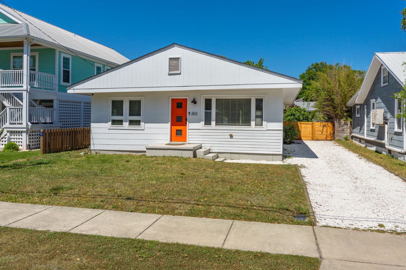 Charming white cottage with bright orange door sits in friendly neighborhood, offering easy parking and welcoming front yard space.