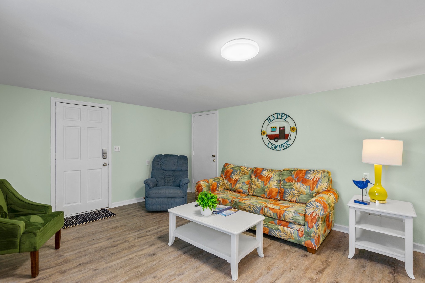 Relax in your cheerful living space with tropical-print sofa, cozy recliner, and Happy Camper charm welcoming you home.