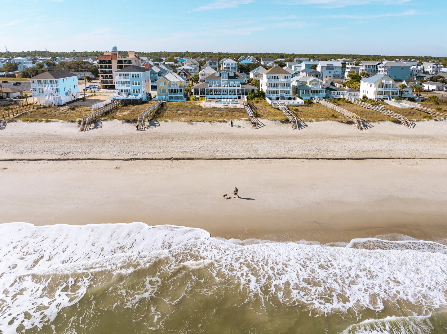 Aerial view of beachfront vacation homes with direct access to pristine sandy shore and gentle ocean waves.