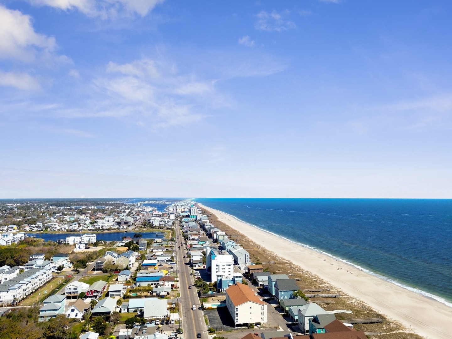 Aerial view of coastal community with pristine sandy beach stretching along turquoise waters and charming beachfront homes.