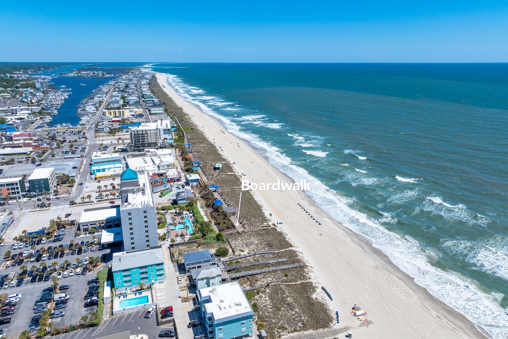 Aerial view of pristine oceanfront coastline with expansive sandy beach and rolling waves meeting a vibrant coastal community.