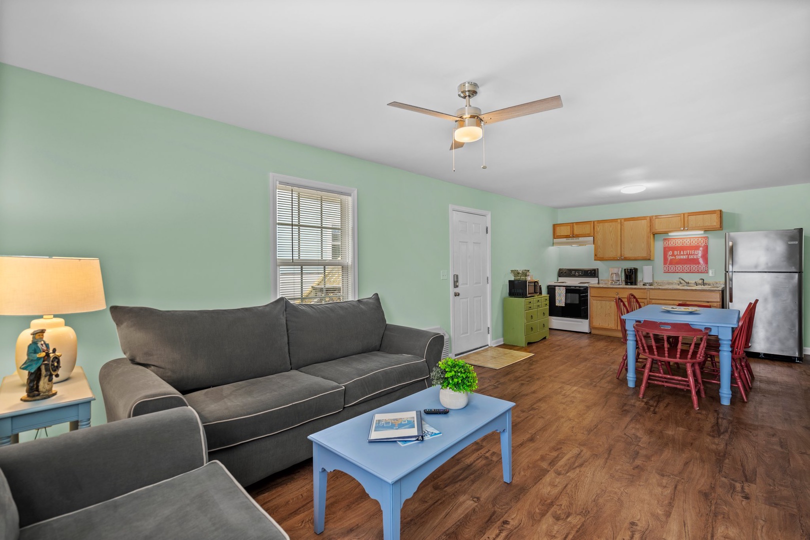 Unwind in your open-concept living space with comfortable gray seating, soothing mint walls, and a full kitchen ready for your culinary adventures.